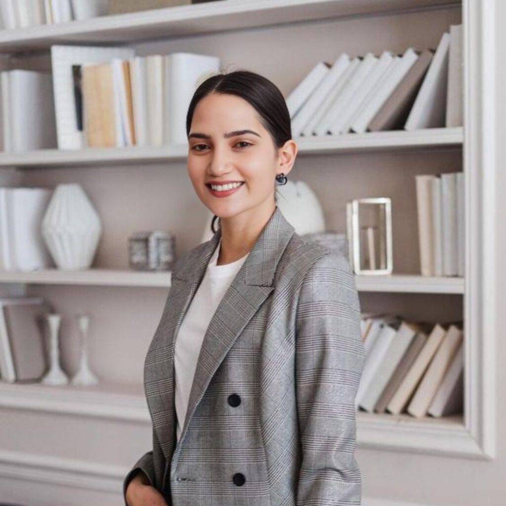 Professional woman in a stylish blazer smiling confidently in front of a bookshelf, representing career success and personal growth.