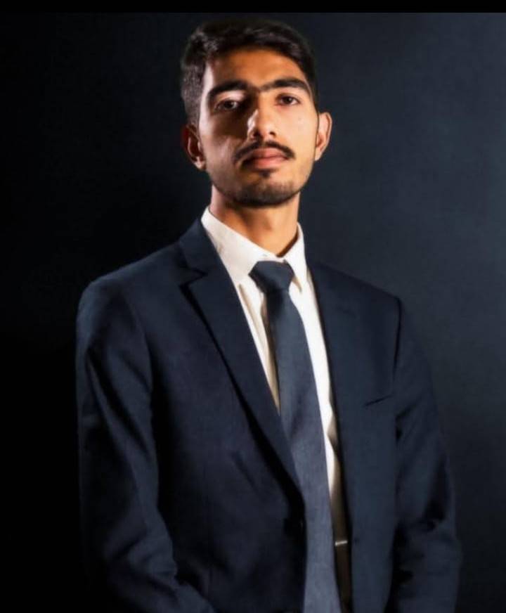 Confident young professional in a suit posing against a dark background, representing leadership and career success.